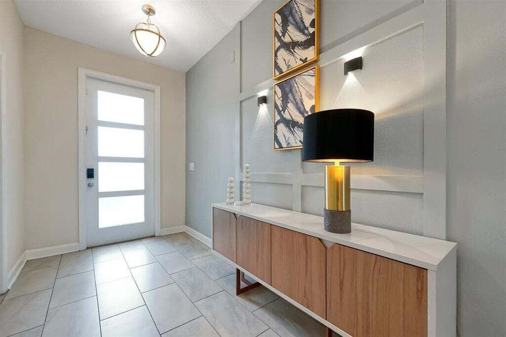 En gang med en hvid dør, en lysarmatur, en vægmonteret lampe og et skab med et spejl.