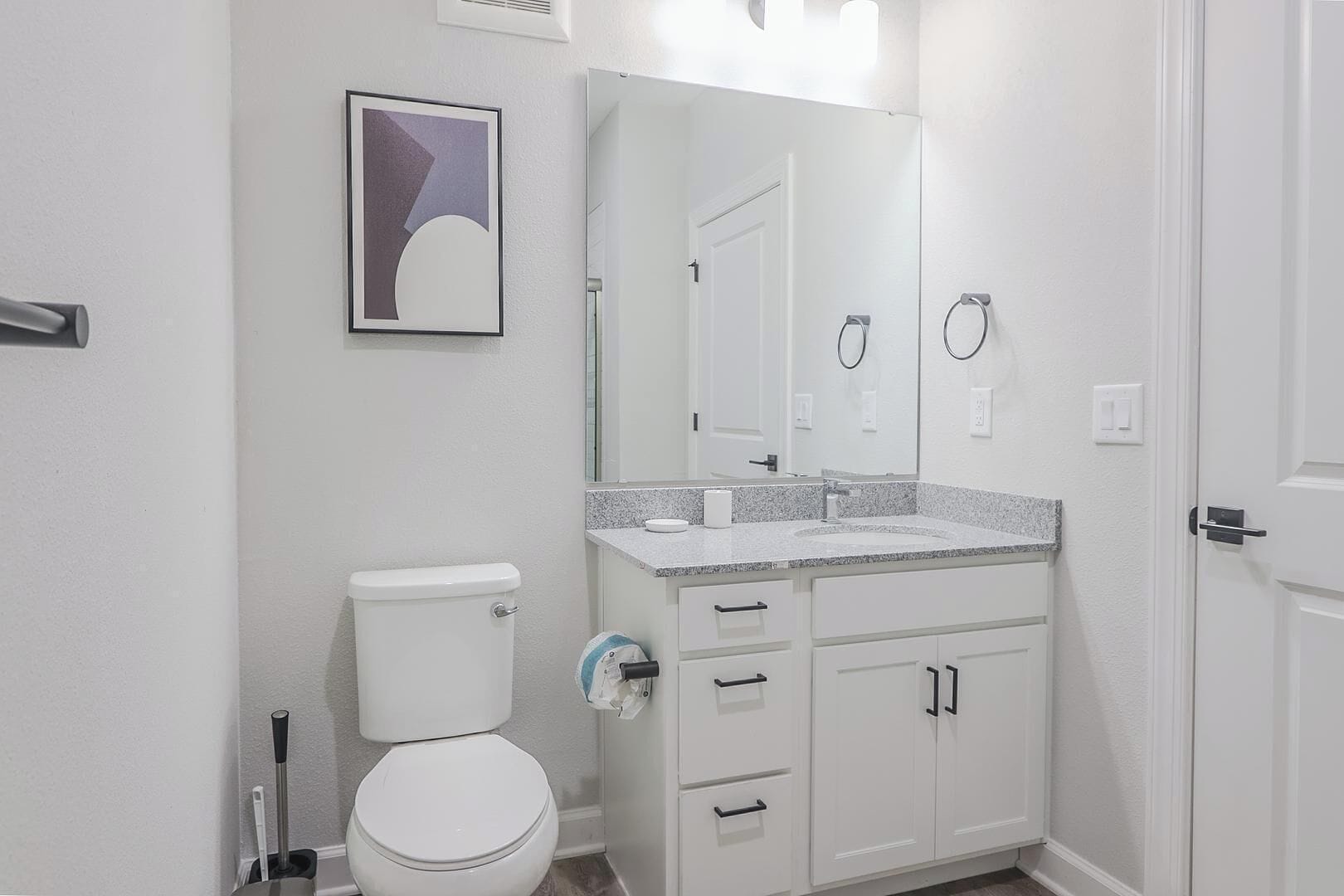 A bathroom with a toilet, sink, mirror, and cabinets.