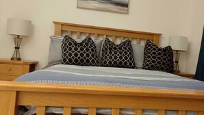 Una cama bien hecha con un cabecero de madera, varios cojines estampados y dos lámparas de noche sobre mesitas de madera.