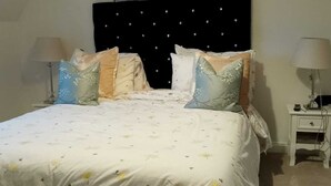 Una cama con colcha blanca estampada con flores, cabecero tapizado negro con diseño de estrellas y dos lámparas de noche.