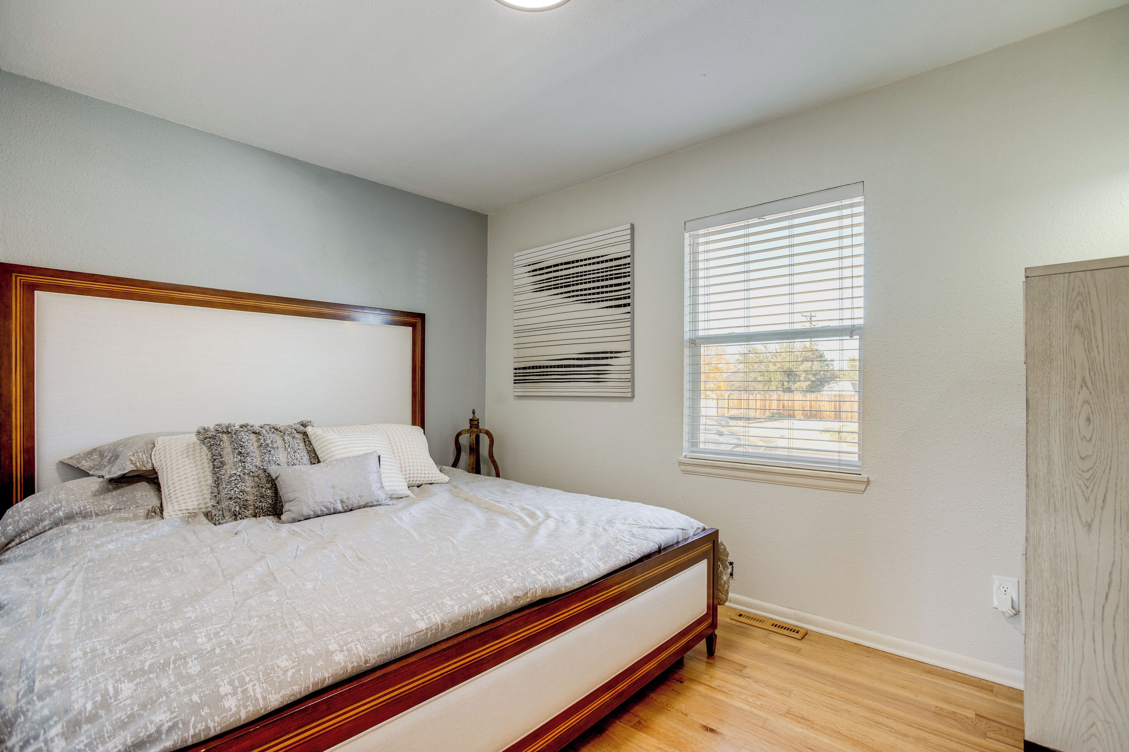 Une chambre à coucher avec un grand lit, deux fenêtres équipées de stores, une tête de lit en bois et une porte.