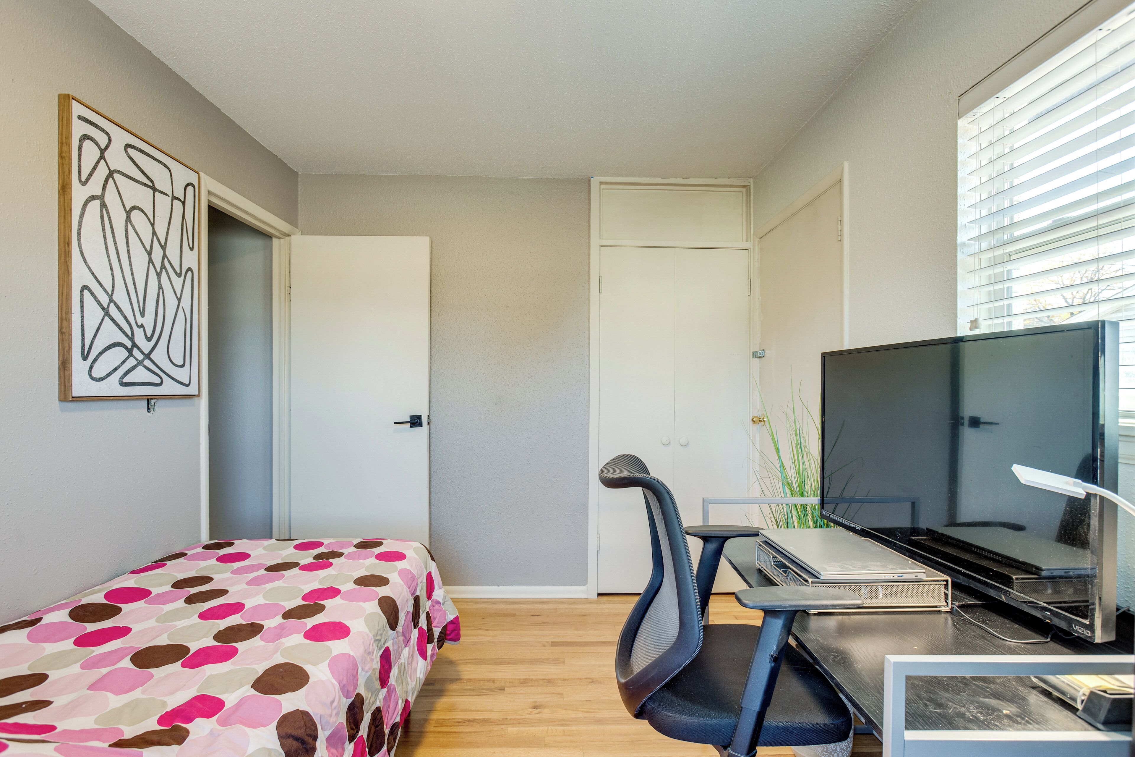 A small, modern room with a bed, desk, and TV.
