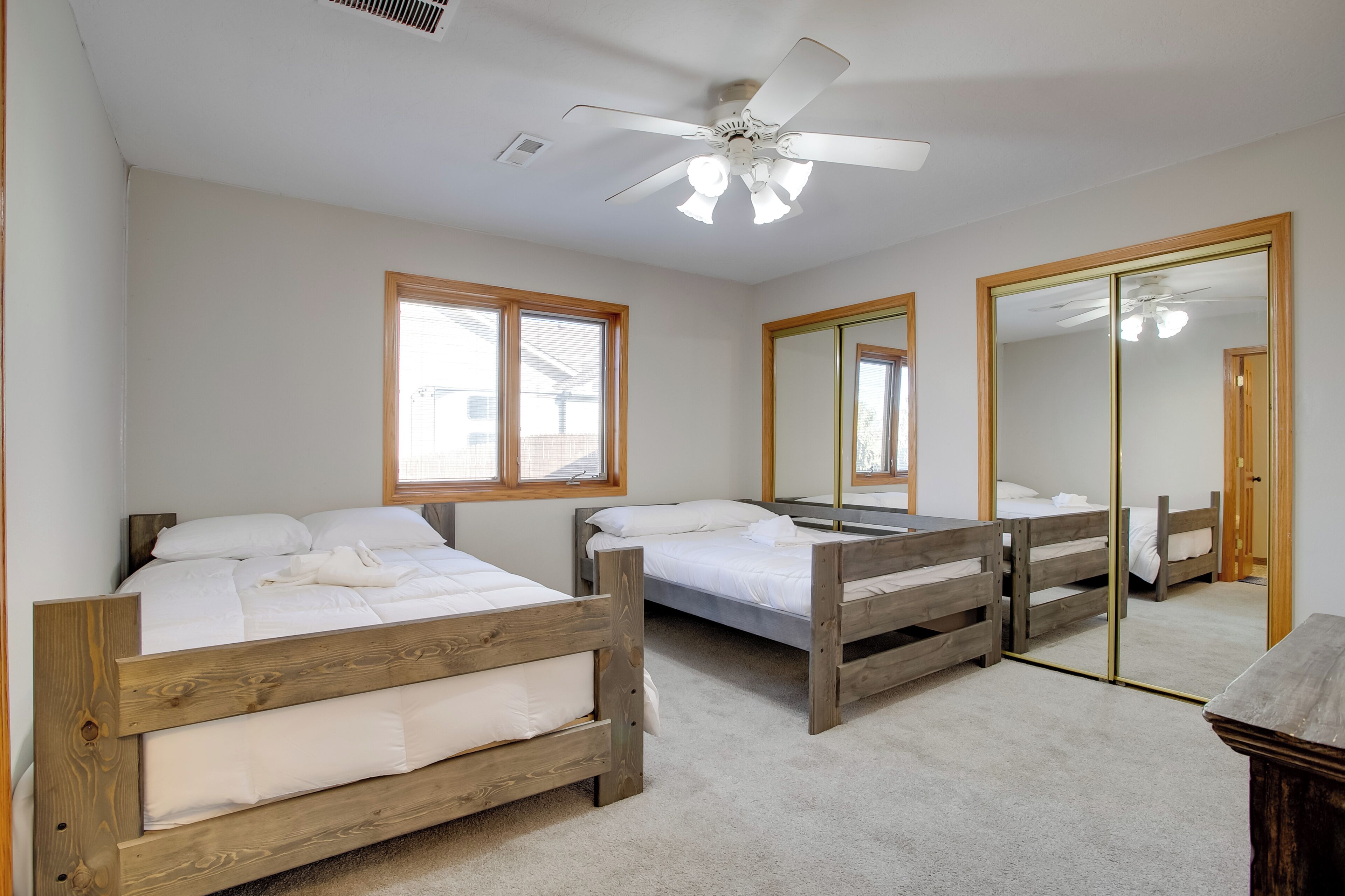 Une chambre avec trois lits superposés en bois, un ventilateur de plafond et de grandes fenêtres.