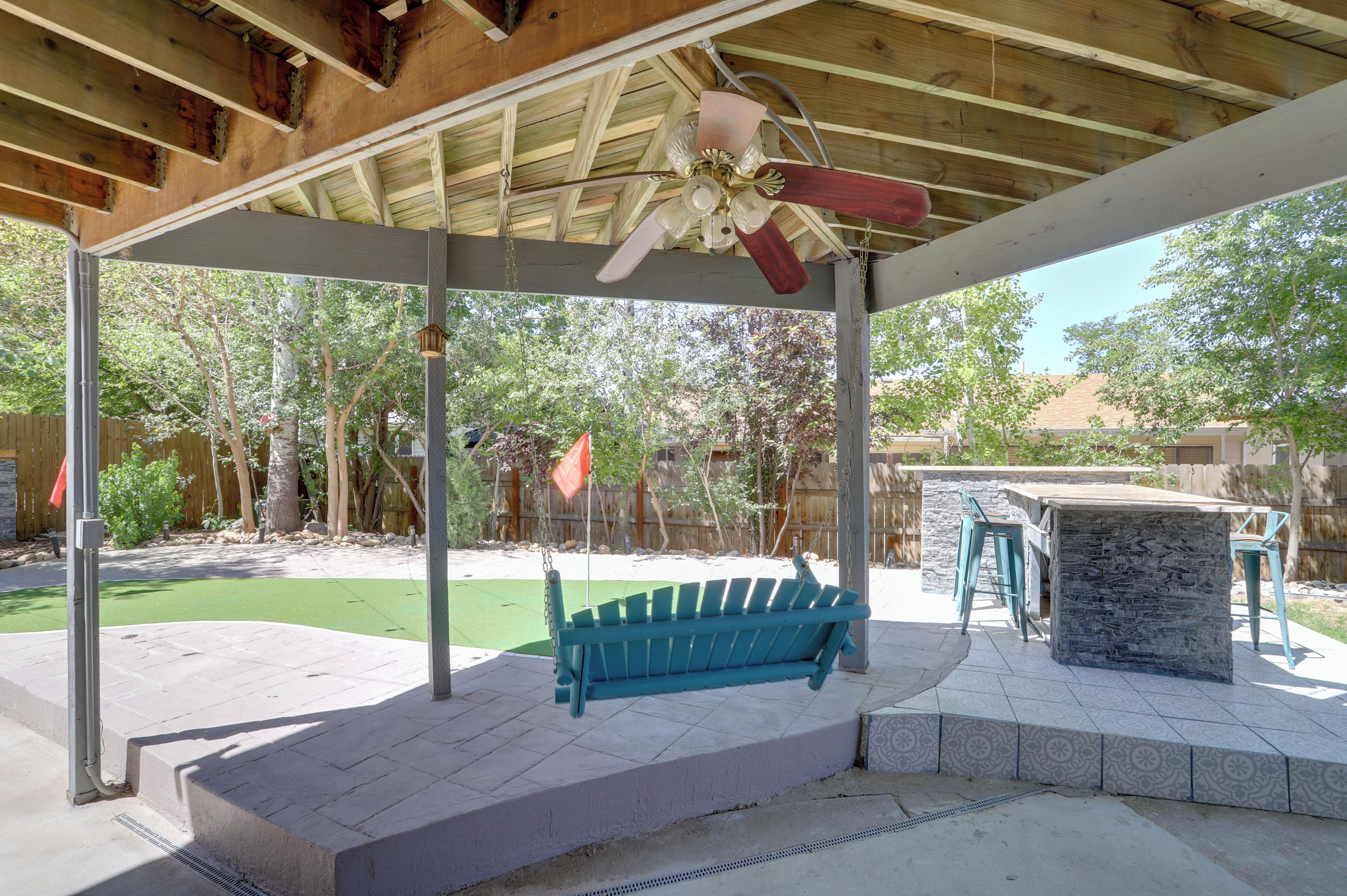 A covered patio with a swing, outdoor seating, and a stone table.