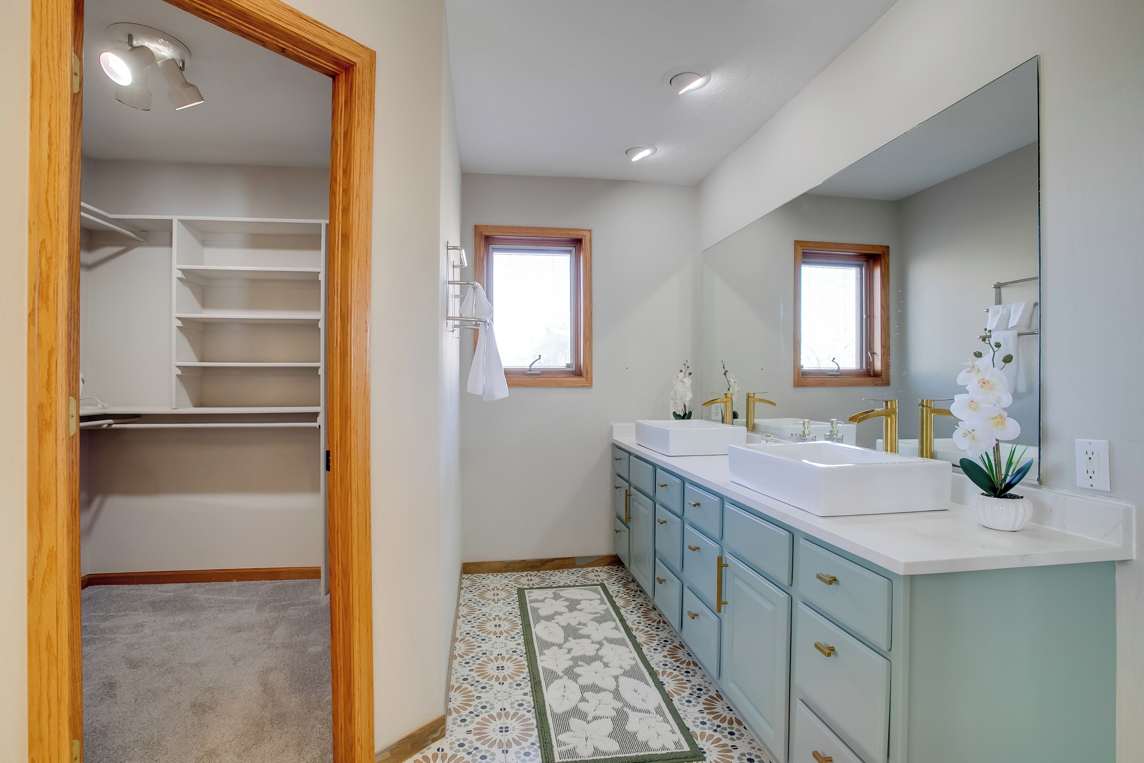 A modern bathroom with a walk-in closet, two sinks, and a large mirror.