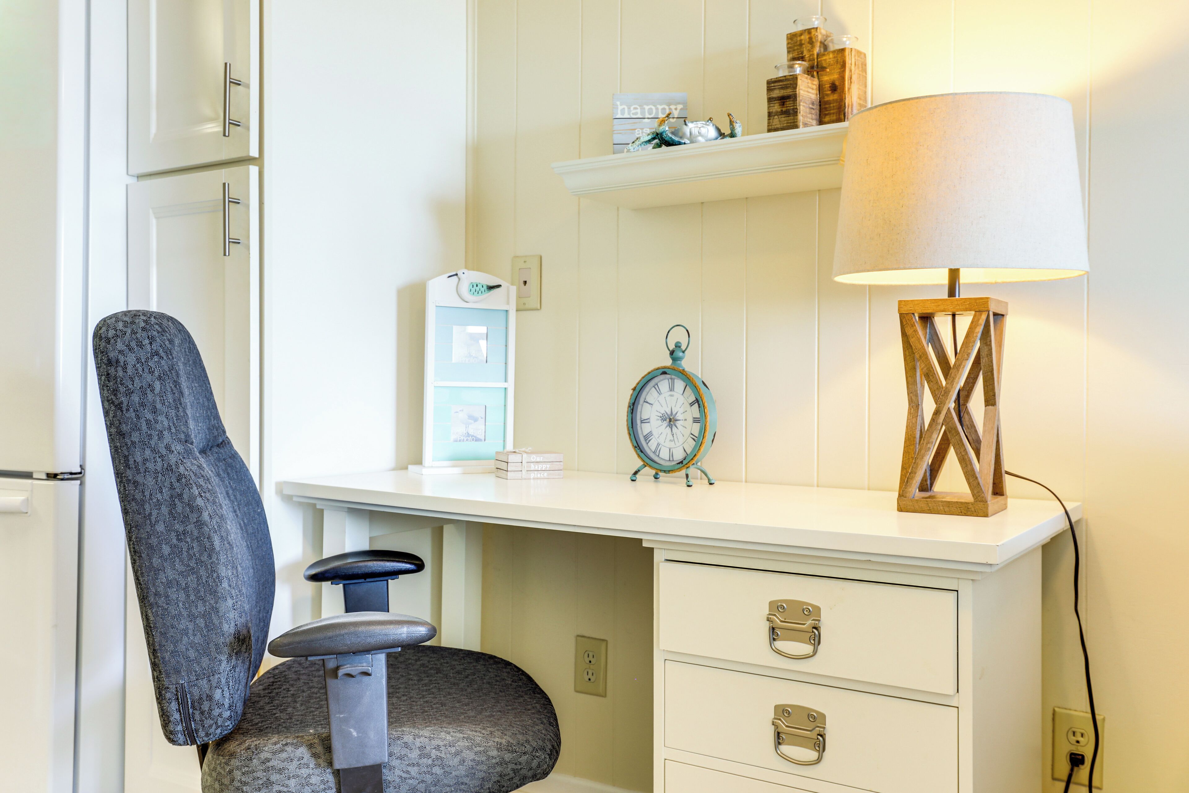 A white desk with drawers, a blue chair, a clock, and a lamp.