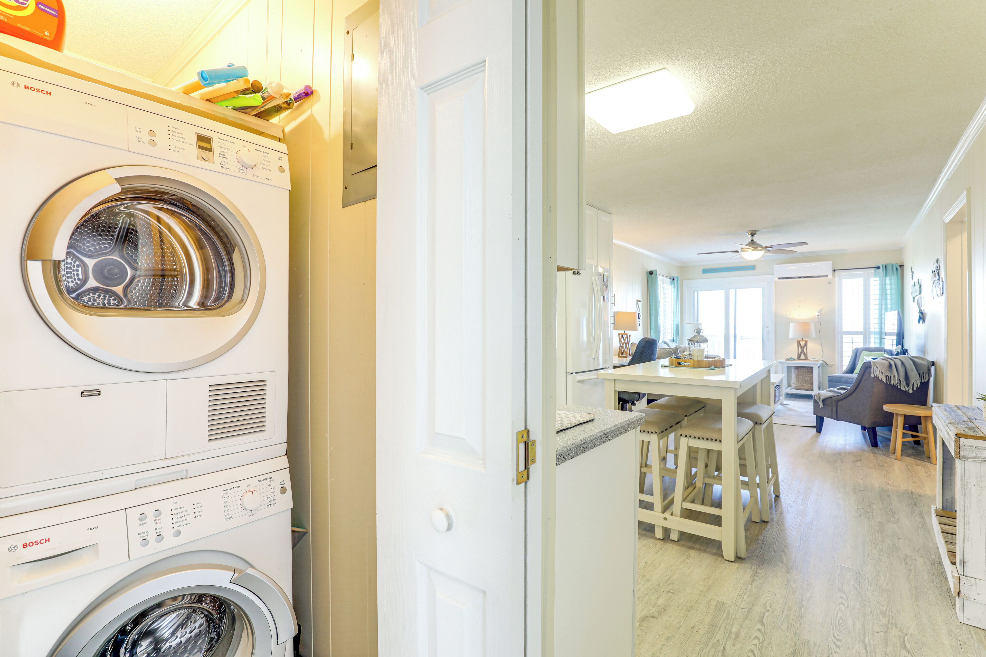 Une buanderie équipée d’un lave-linge et d’un sèche-linge Bosch, un coin repas avec une table et des chaises, et un salon avec un canapé et un ventilateur de plafond.