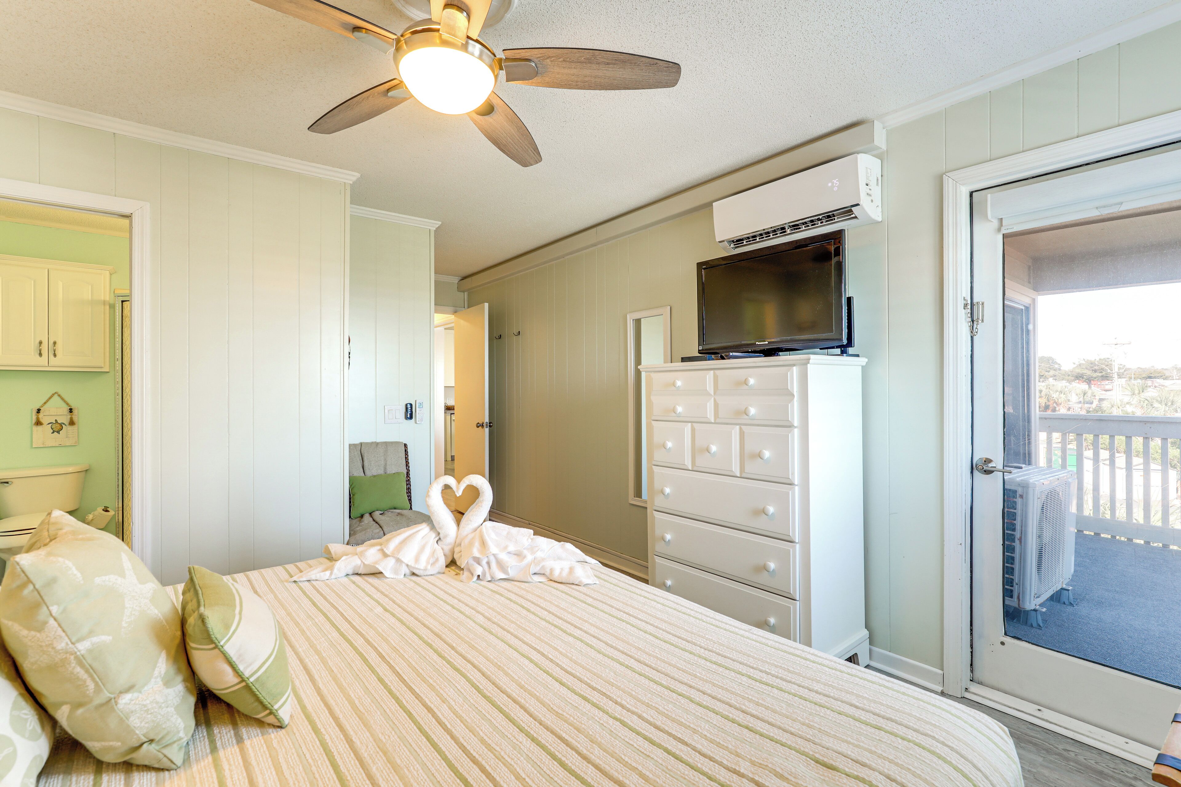 A bedroom with a bed, pillows, a dresser, a television, and a ceiling fan.