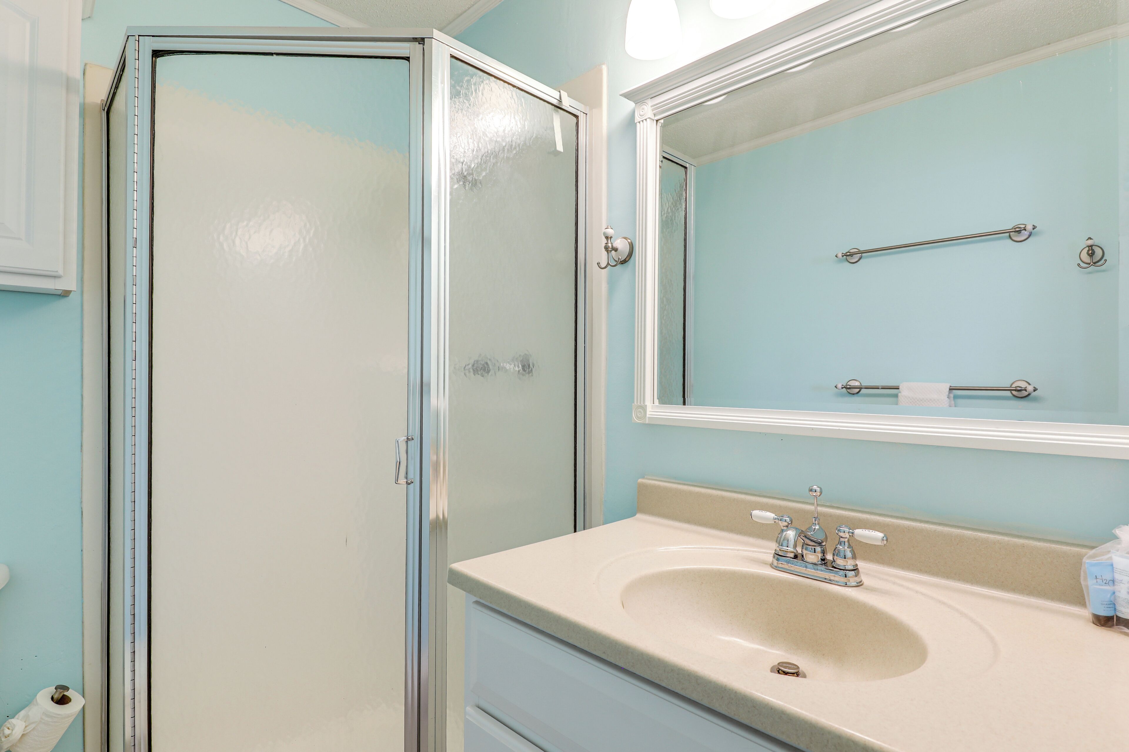A bathroom with a glass shower enclosure, a sink with a mirror above it, and a towel rack.