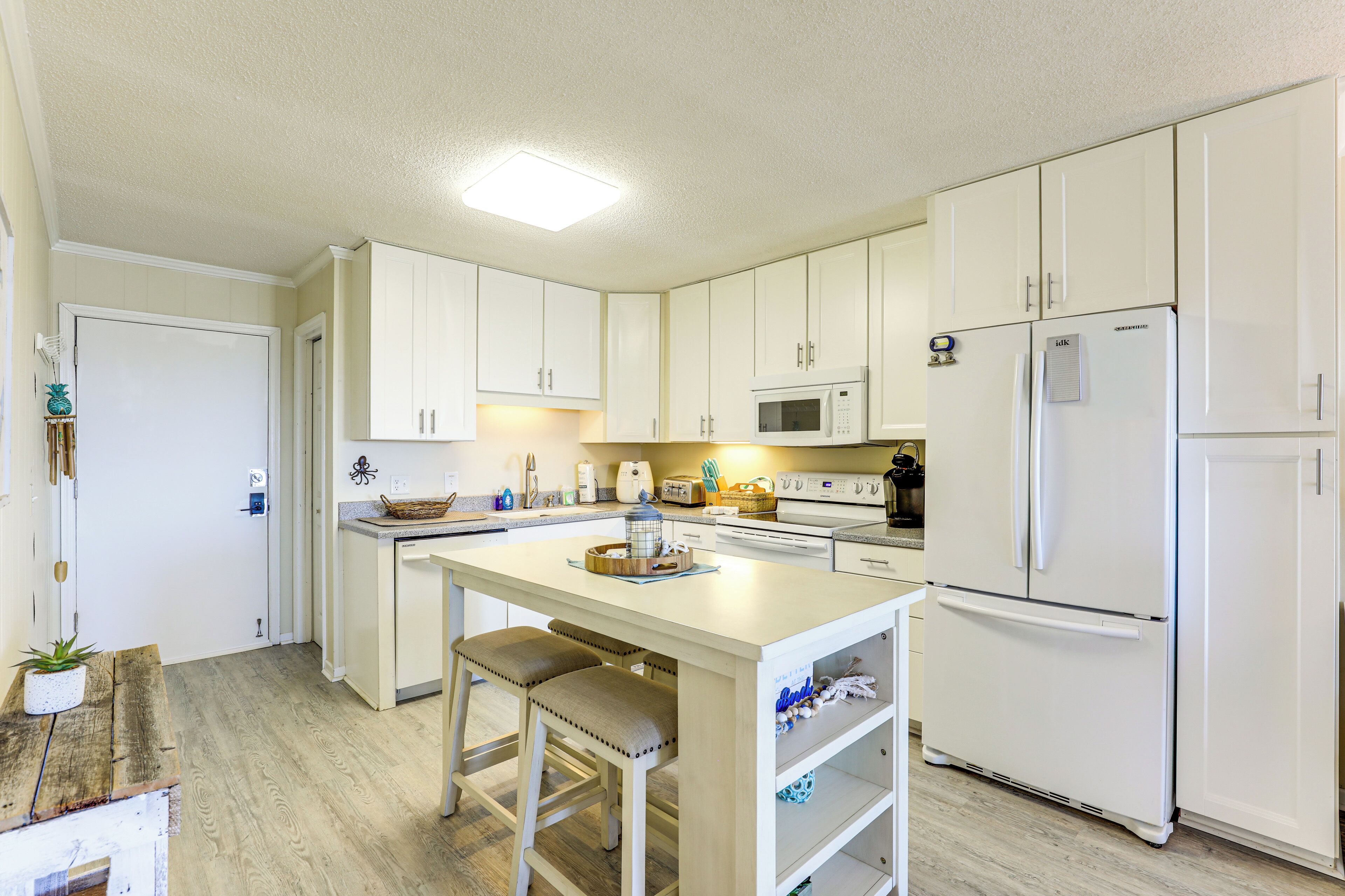 A compact kitchen with white cabinets, a central island with stools, a microwave, and a refrigerator.