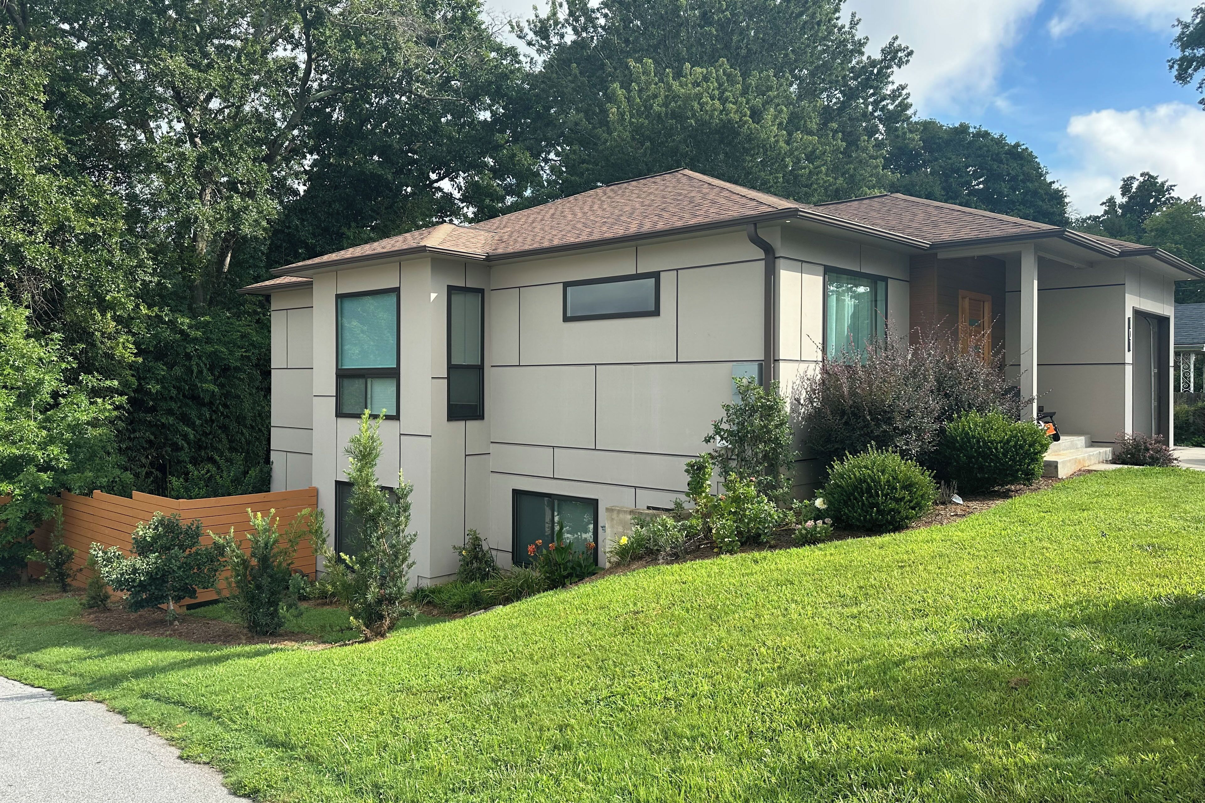 A modern two-story house with a sloped roof, large windows, and a well-maintained lawn.