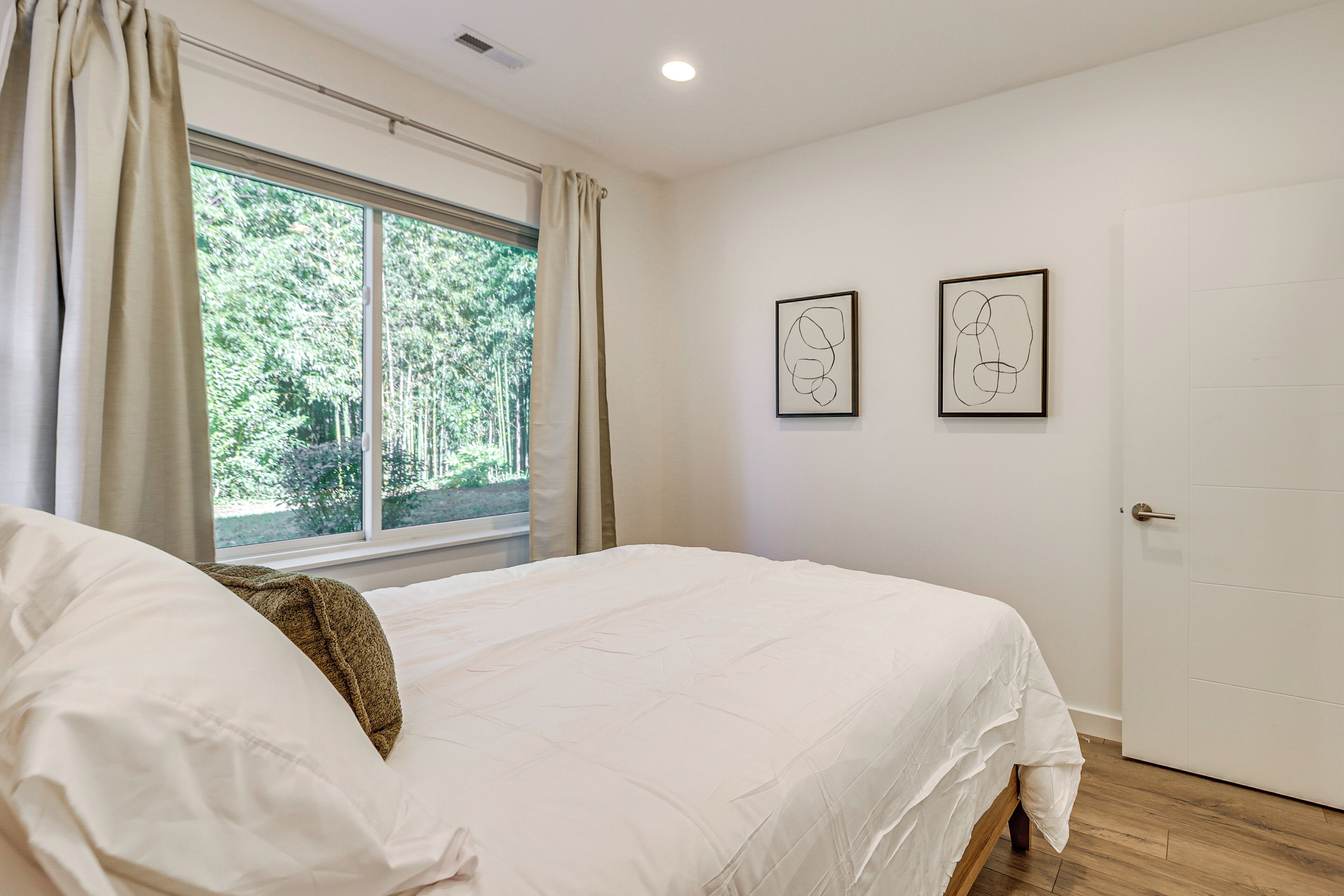 A bedroom with a large bed, a window with curtains, and two framed abstract artworks on the wall.