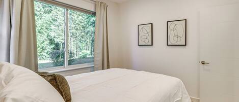 A bedroom with a large bed, a window with curtains, and two framed abstract artworks on the wall.