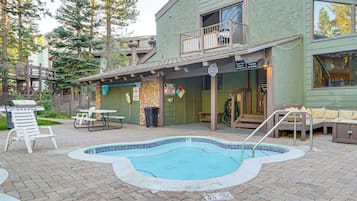 Uma área de piscina com hidromassagem, área de estar ao ar livre e um edifício com varanda.