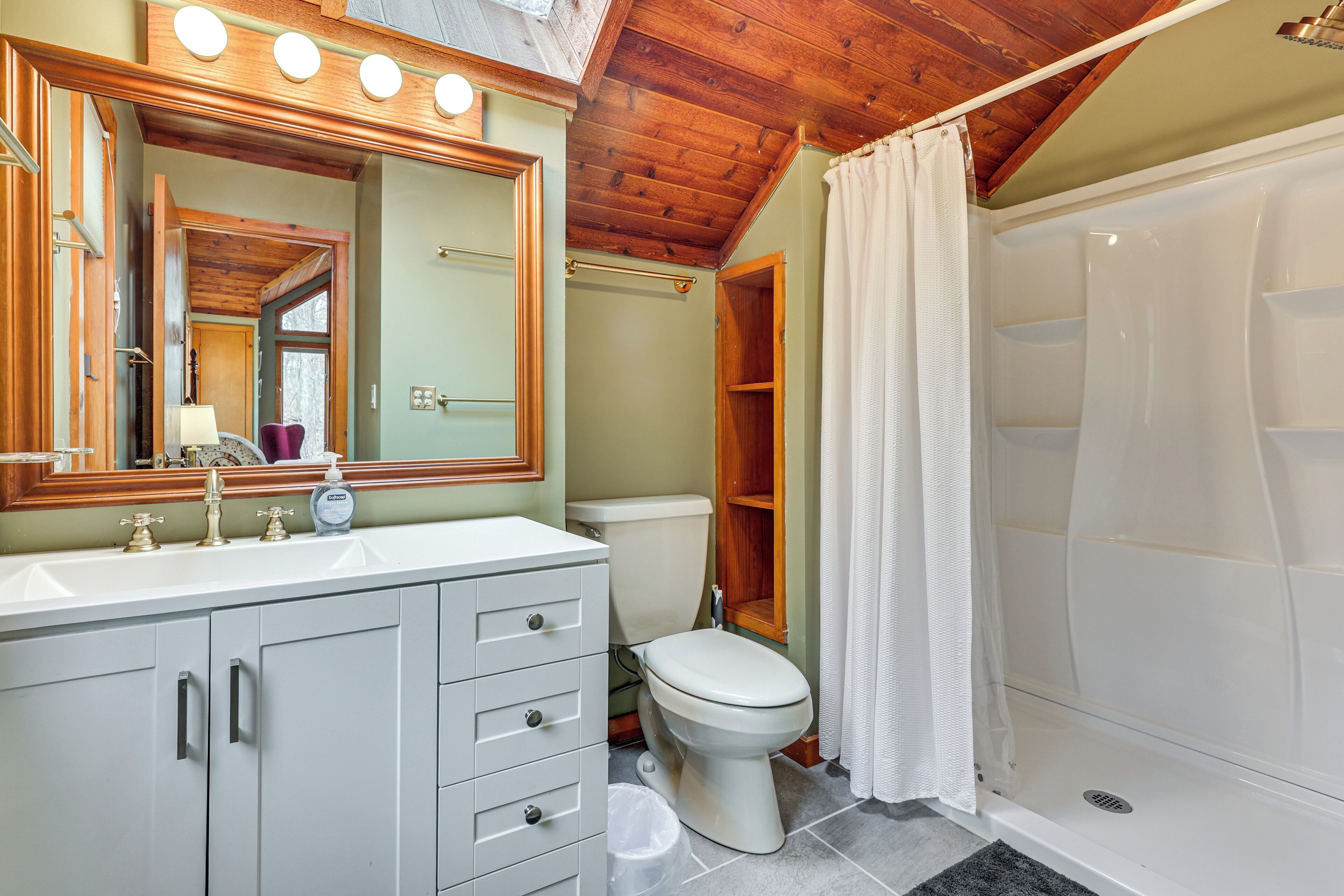 Un bagno con soffitto in legno, un lavandino bianco, un WC e una doccia con tenda bianca.