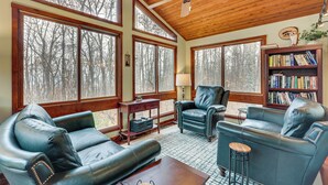 A spacious living room with leather sofas, a wooden ceiling, large windows, and a bookshelf. - Grand Wintergreen Resort Home w/ Hot Tub! (Nellysford)