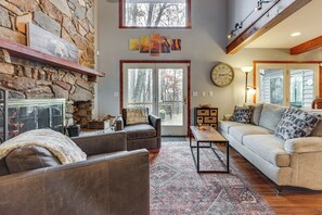 A cozy living room with a stone fireplace, leather sofas, and a large window overlooking a deck. - Grand Wintergreen Resort Home w/ Hot Tub! (Nellysford)