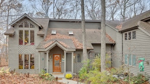 A two-story house with a front porch, a chimney, and a small garden area with a tree and shrubs. - Grand Wintergreen Resort Home w/ Hot Tub! (Nellysford)