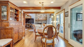 A dining area with a wooden table and chairs, a built-in cabinet, and a stone fireplace. - Grand Wintergreen Resort Home w/ Hot Tub! (Nellysford)
