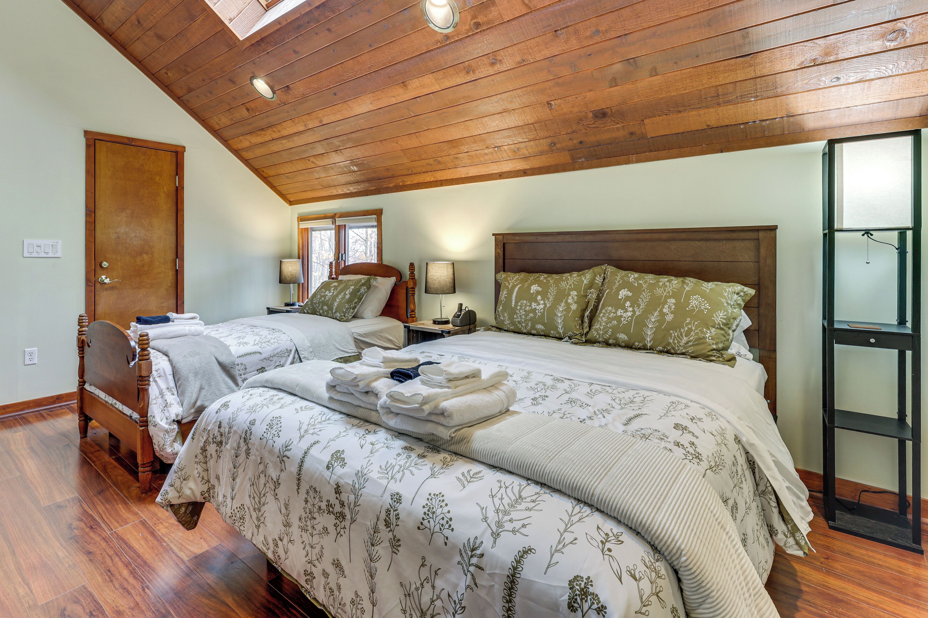 A bedroom with two beds, wooden ceiling beams, and a skylight.