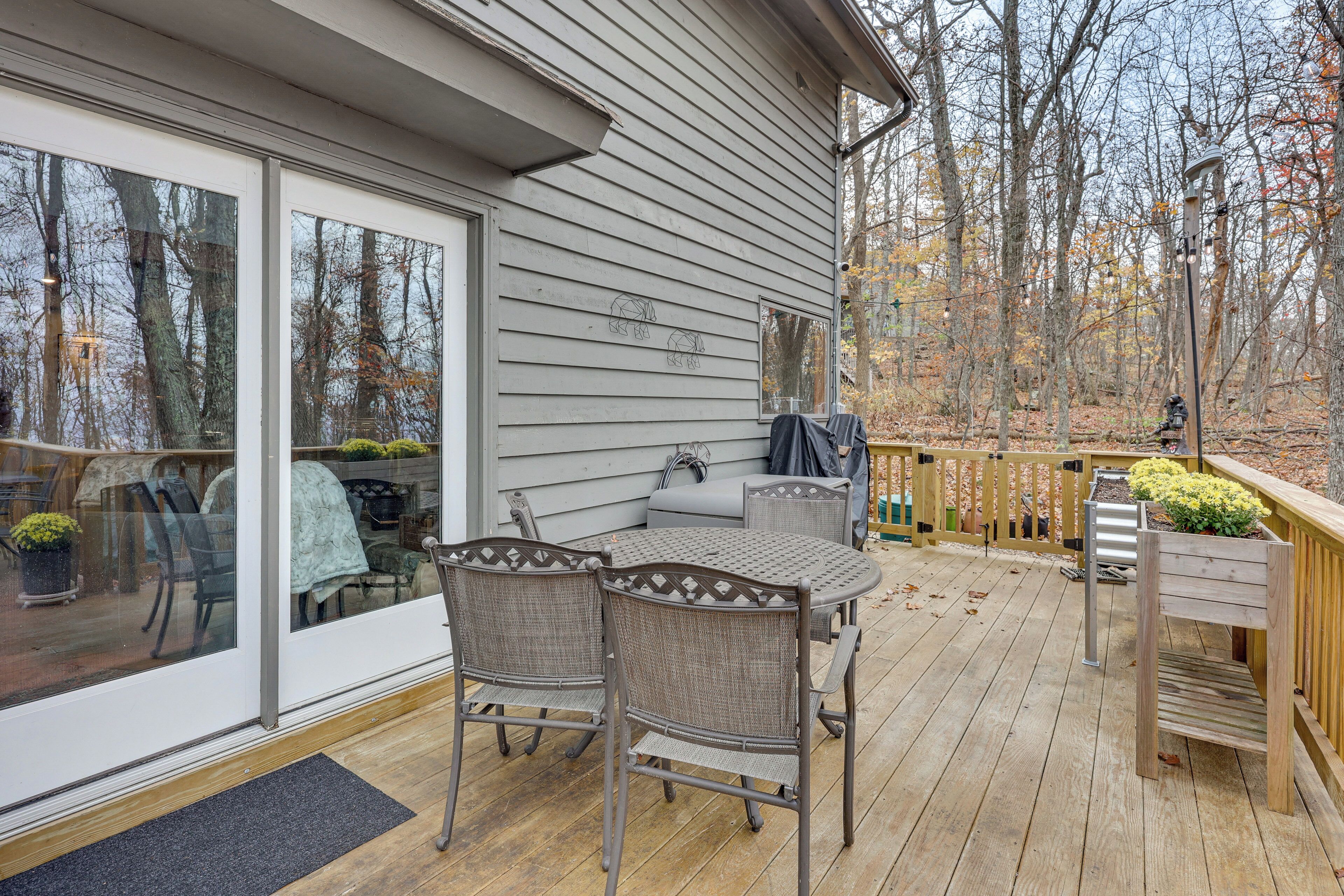 A covered patio with a table and chairs, a wooden deck, and a view of trees.