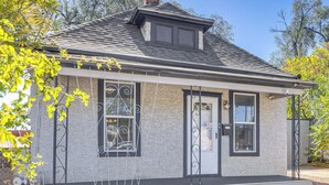 A small, single-story building with a gabled roof, a front door, and two windows with decorative ironwork.