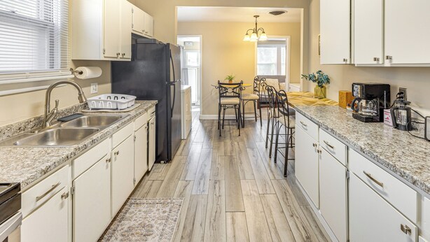 A kitchen with white cabinets, a black refrigerator, a sink, and a dining area with a table and chairs.