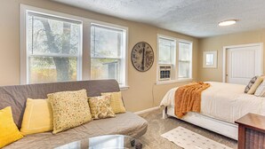 A bedroom with a bed, a sofa, a glass table, and a clock on the wall.
