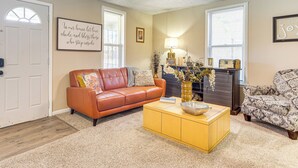A living room with a brown leather sofa, a yellow coffee table, and a patterned armchair. There is a fireplace with decorative items and a lamp.