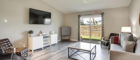A modern living room with a flat-screen TV, a sofa, a coffee table, and a sliding glass door leading to a patio.