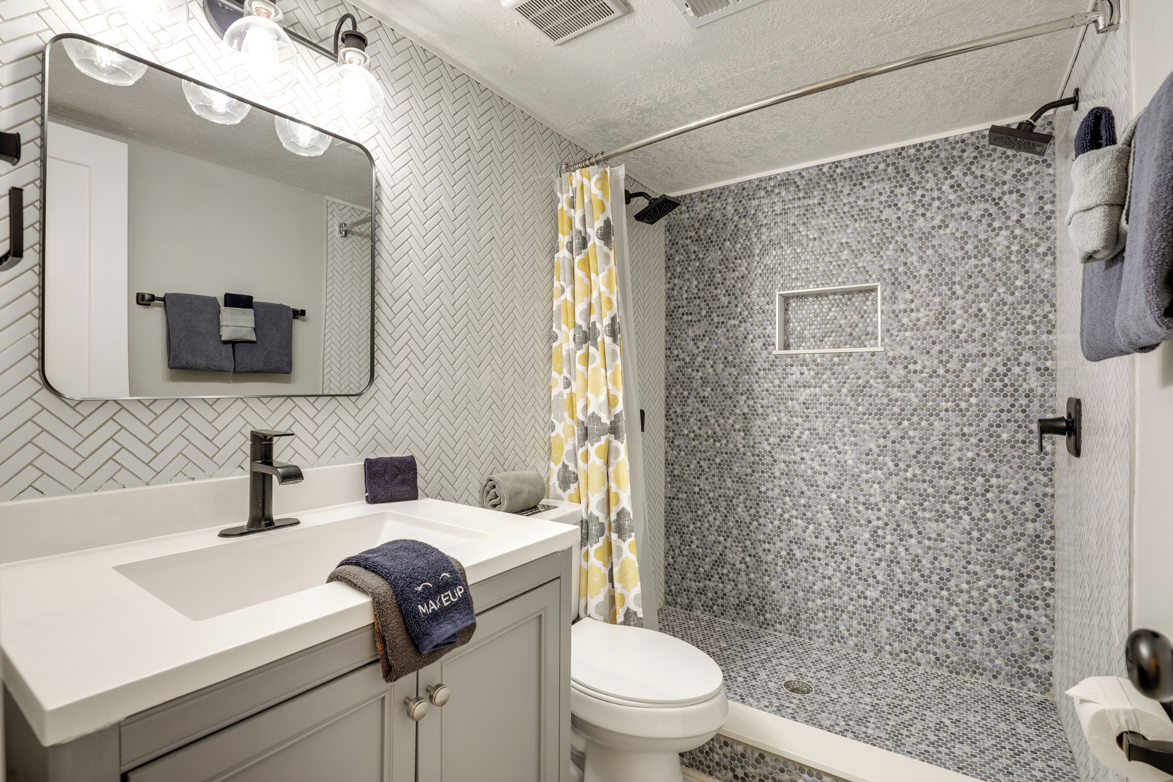Un bagno con lavandino bianco, specchio e WC. È presente una doccia con porta in vetro decorato.
