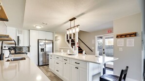 Une cuisine moderne avec des meubles blancs, un réfrigérateur en acier inoxydable, un îlot central intégré et un escalier menant à un autre niveau.
