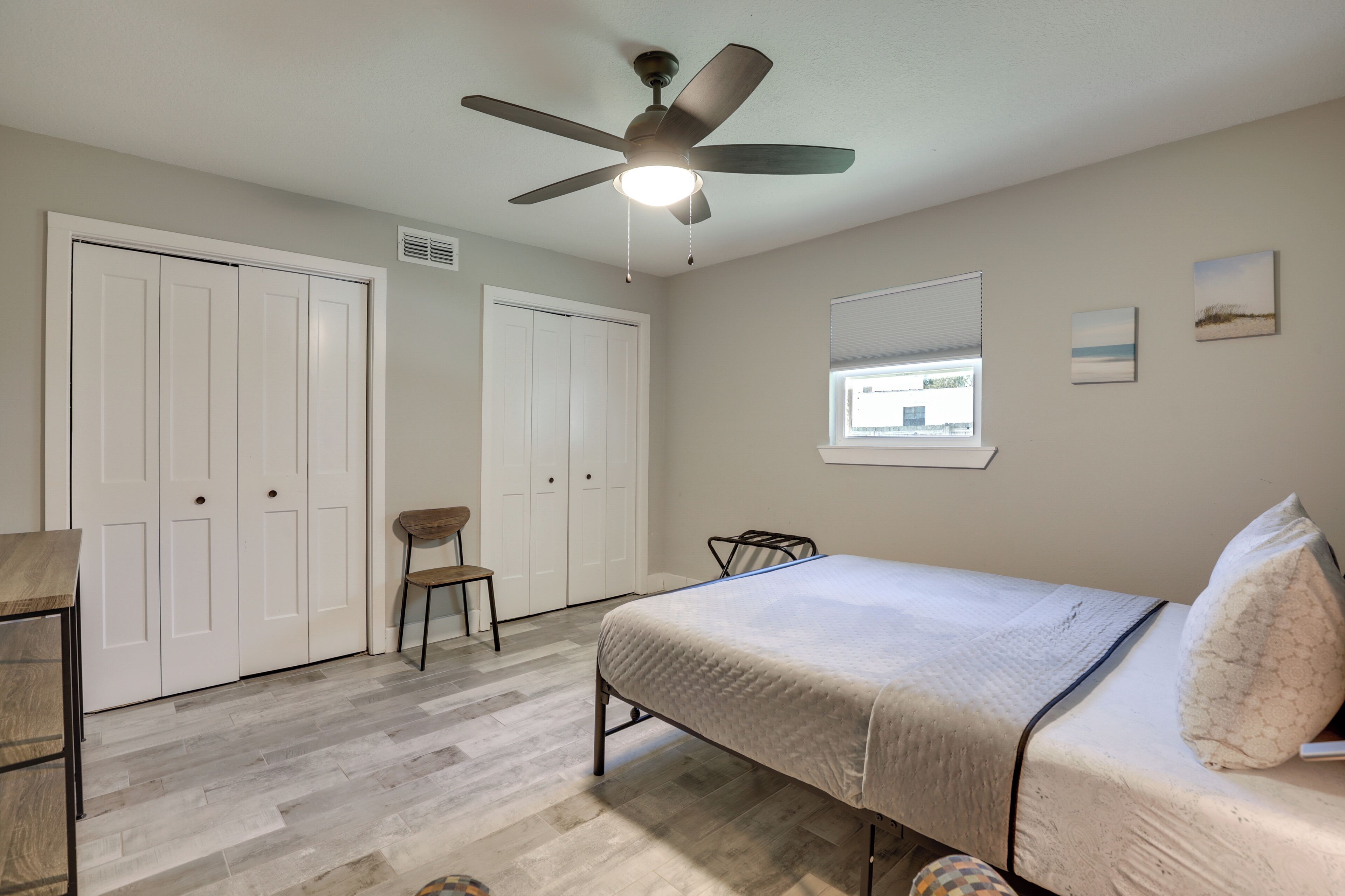 A bedroom with a bed, a ceiling fan, a window, and a chair.
