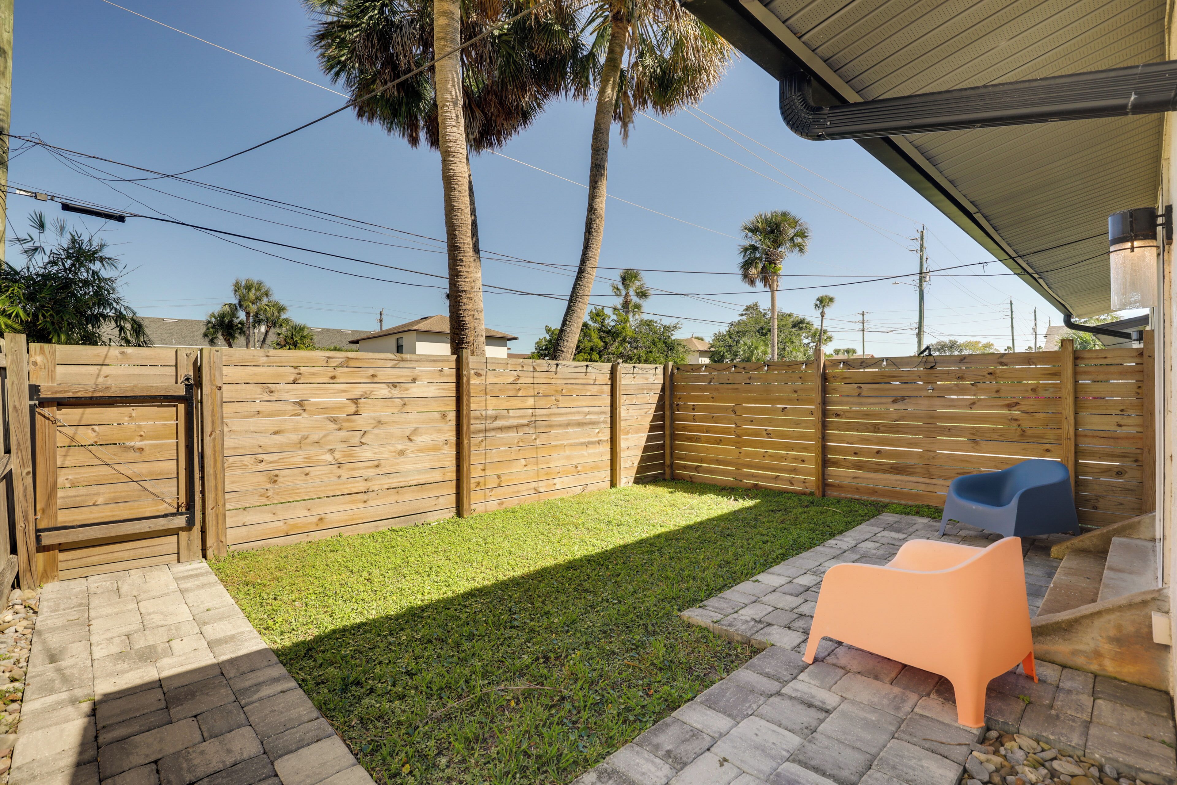 A backyard with a wooden fence, a grassy area, and two plastic chairs.