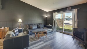 A modern living room with a sofa, a coffee table, and a TV. There is a door leading to an outdoor area. - Stylish & Walkable! Pet-friendly St Augustine Gem! (St. Augustine)