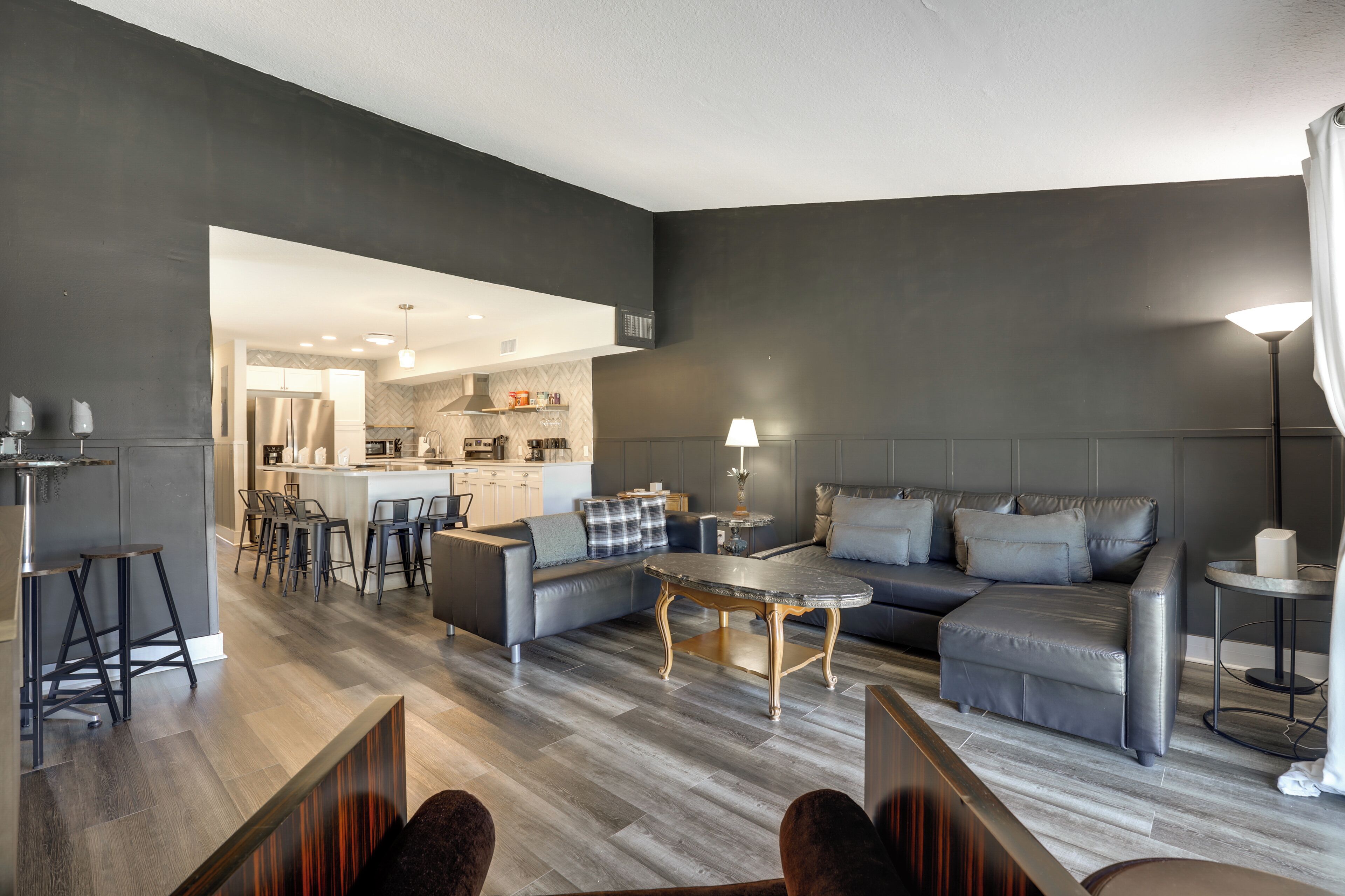 Uma sala de estar moderna com um sofá cinzento, uma mesa de centro e um espaço de jantar com banquetas.