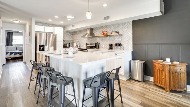 A modern kitchen with a large island, bar stools, and a wooden cabinet. - Stylish & Walkable! Pet-friendly St Augustine Gem! (St. Augustine)