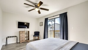 A bedroom with a bed, a ceiling fan, a TV, a chair, a desk, and a window with curtains. - Stylish & Walkable! Pet-friendly St Augustine Gem! (St. Augustine)