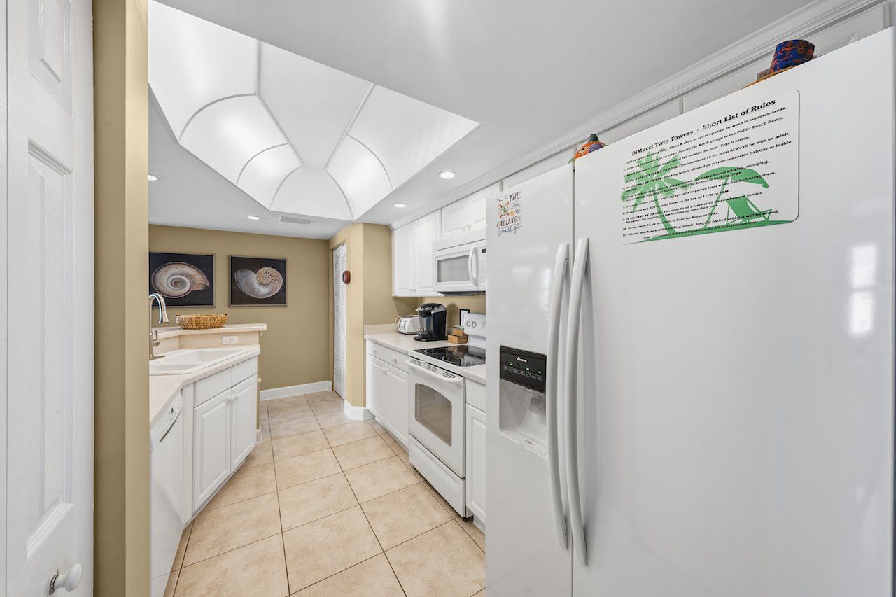 Cocina moderna con armarios blancos, horno empotrado, microondas y refrigerador con un cartel de 'Lista Corta de Reglas'.