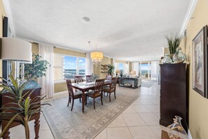 A spacious dining area with a large table and chairs, a chandelier, and a view of the ocean through large windows. - 701 Twin Towers in Daytona Beach Shores, FL (Daytona Beach Shores)