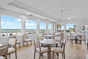 A spacious dining area with large windows overlooking the beach, featuring wooden tables and chairs. - 701 Twin Towers - Daytona Beach Oceanfront Vacations, Inc (Daytona Beach Shores)