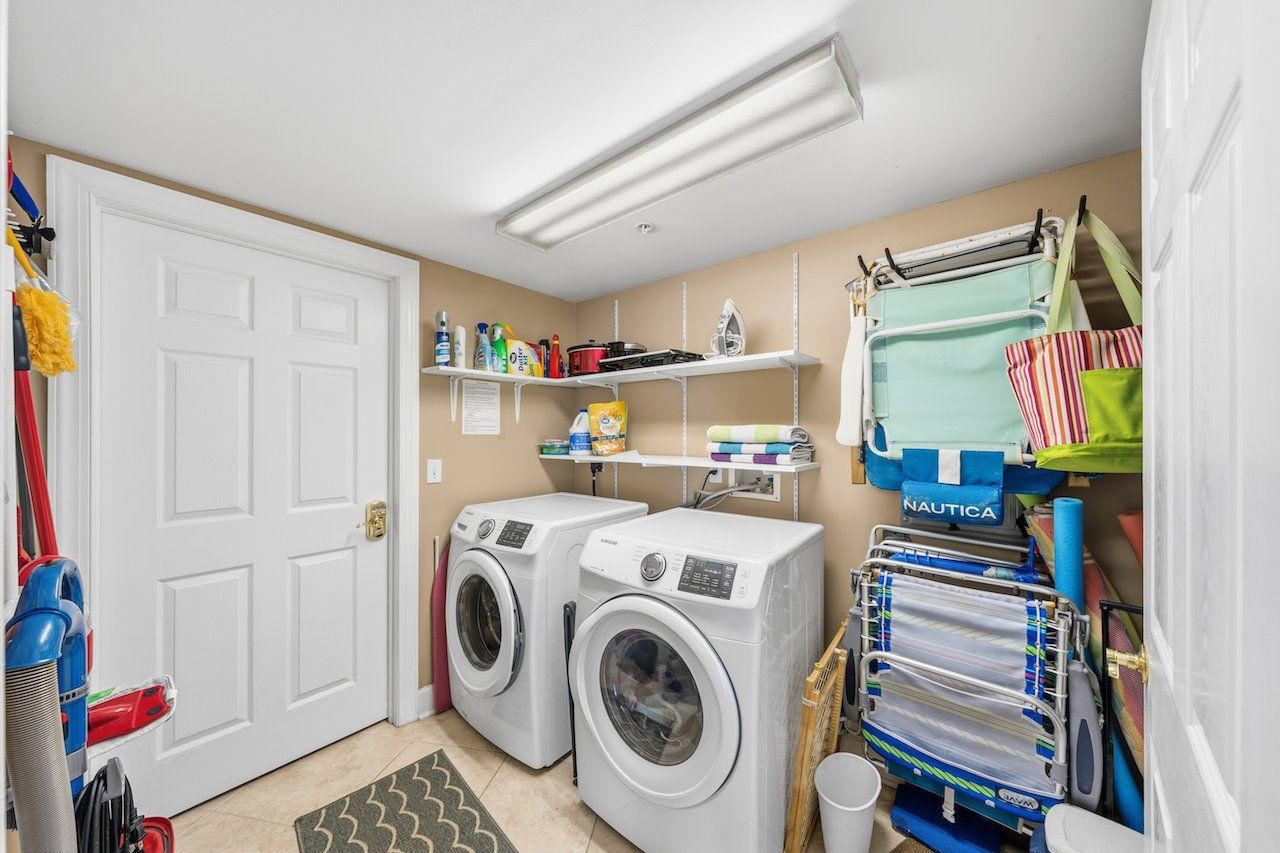 A laundry room with two front-loading washing machines, shelves with cleaning supplies, and a drying rack.