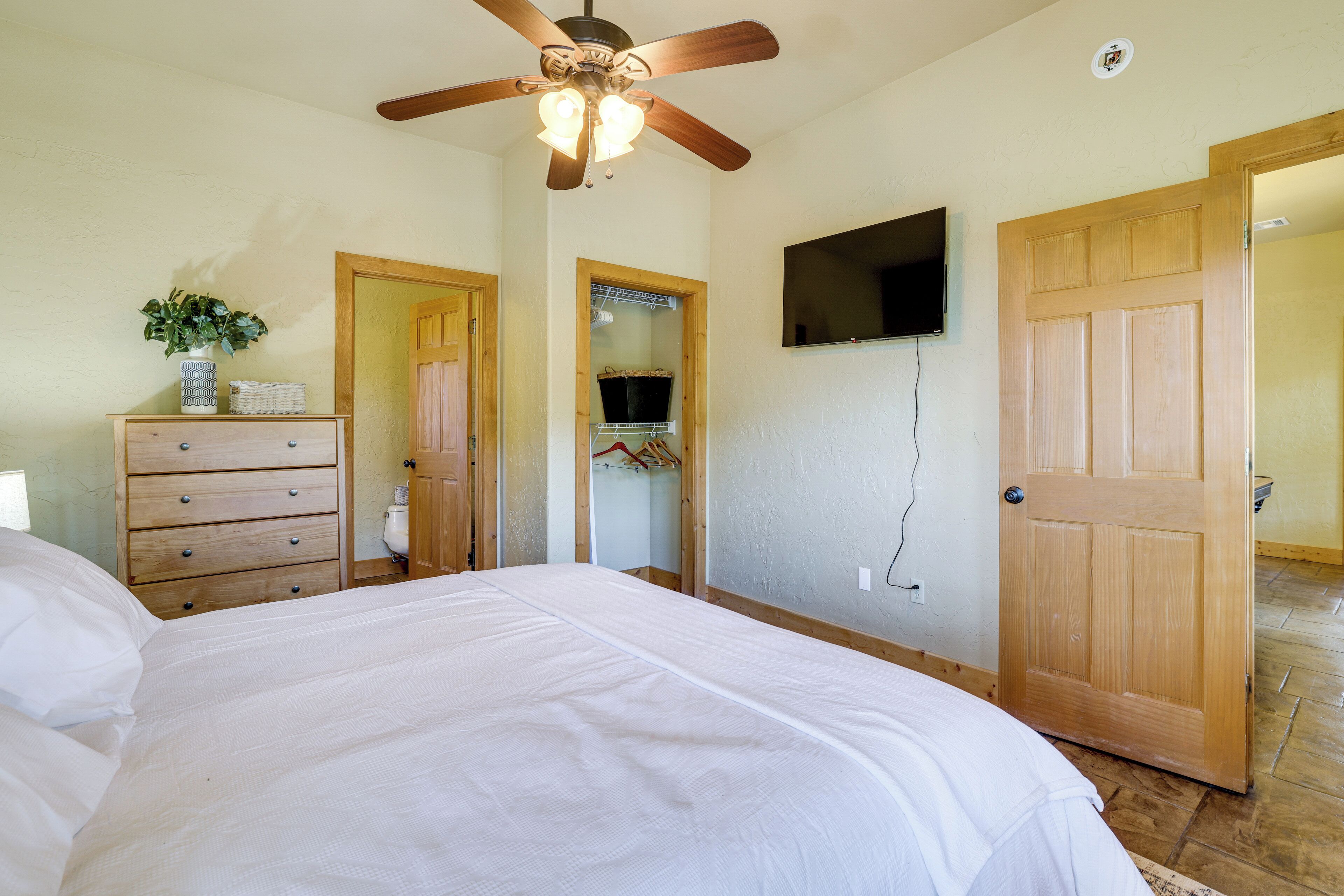 Une chambre à coucher avec un lit, une commode en bois, un placard et un ventilateur de plafond.