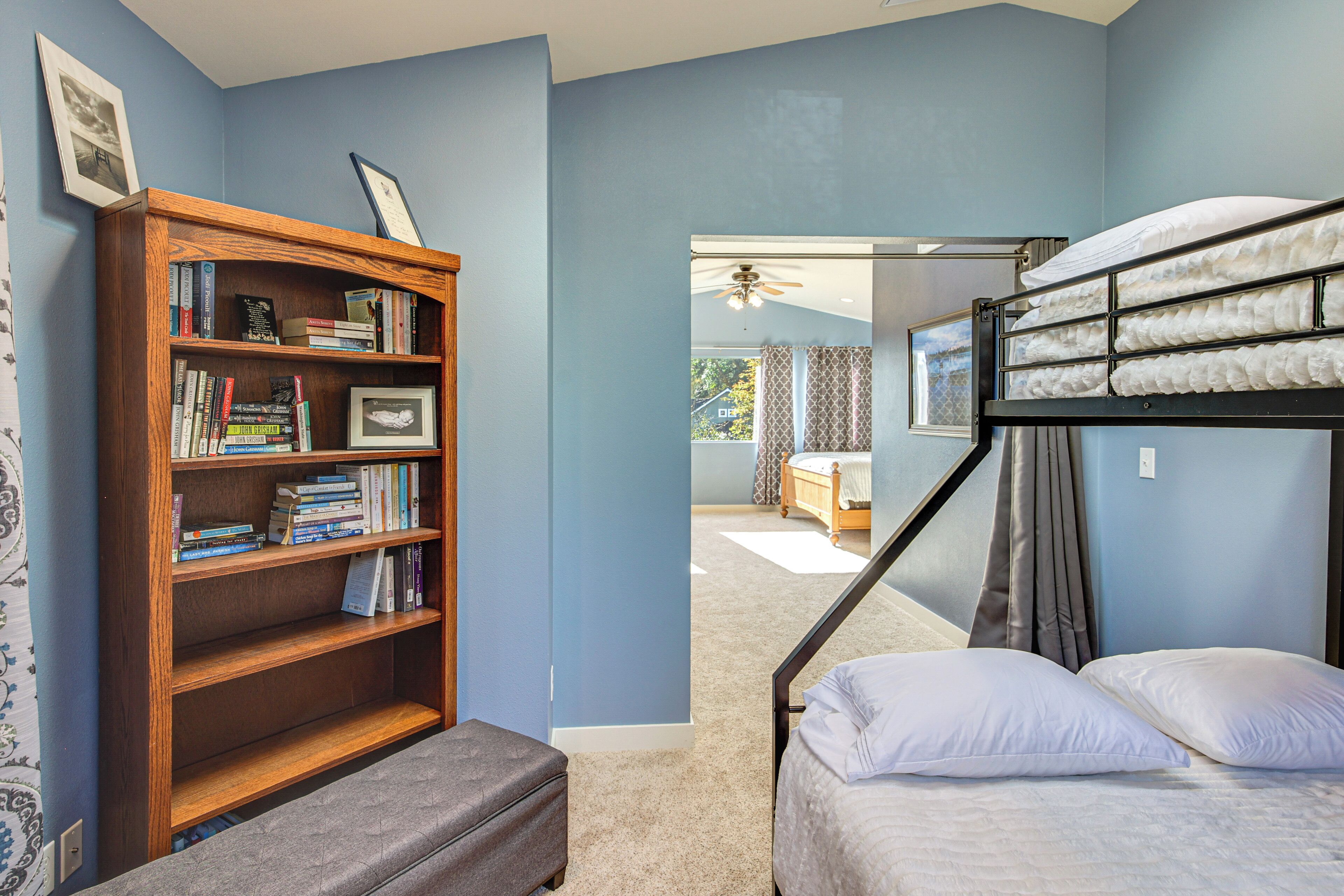 A bedroom with a bunk bed, a wooden bookshelf, and a view of another room through a glass door.