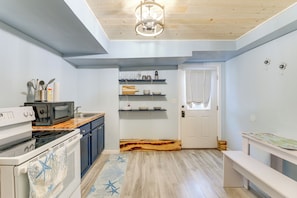 Una cucina compatta con forno a microonde, fornello e piano di lavoro in legno. Ci sono scaffali sopra il bancone e una porta con tenda.