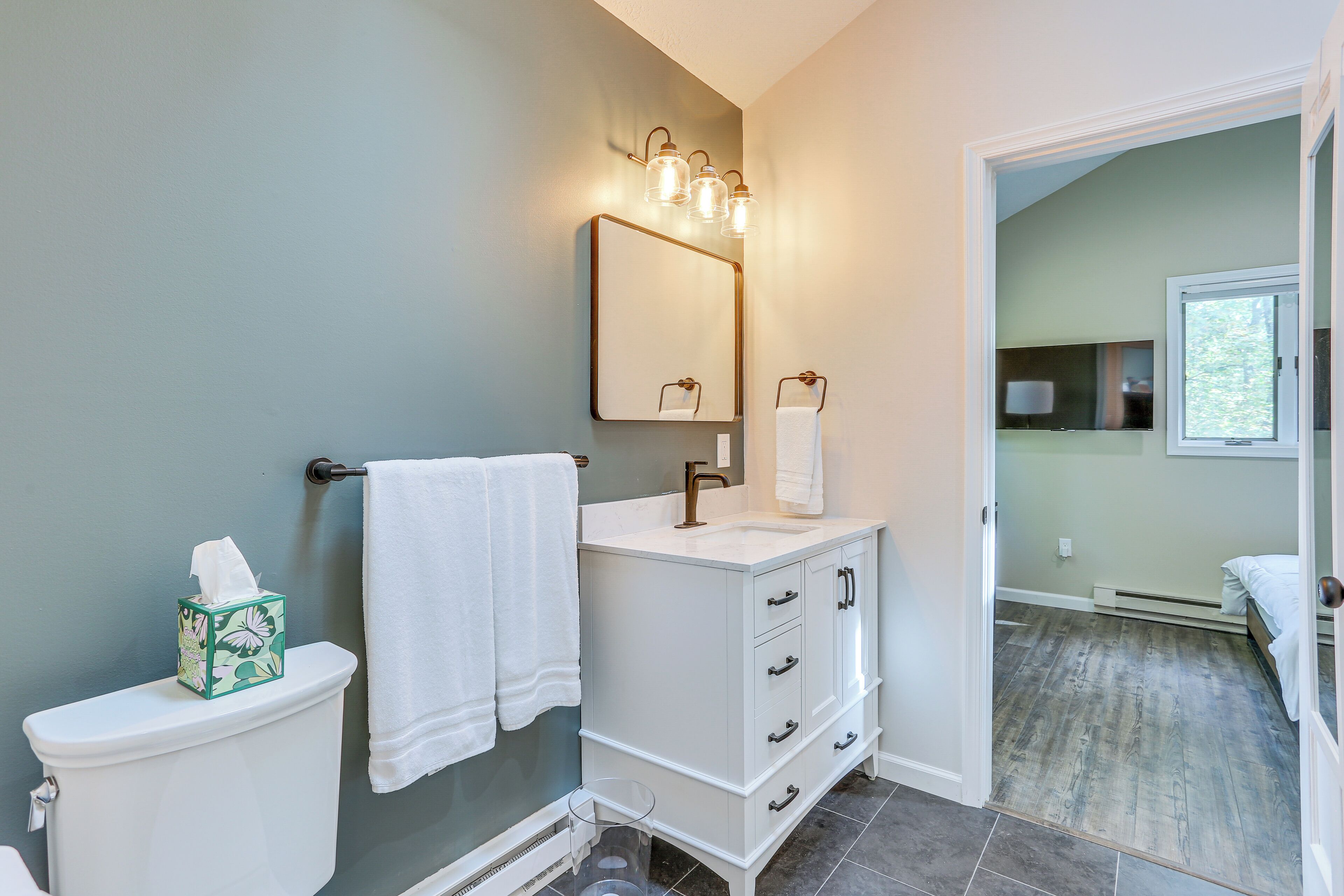 A bathroom with a toilet, a sink with a mirror, and a towel hanging on the wall.