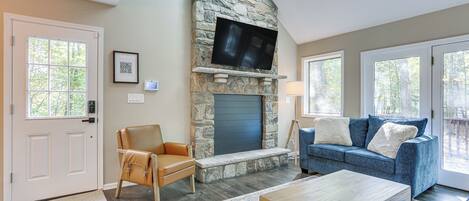 Una sala de estar con chimenea de piedra, televisor de pantalla plana, sofá azul y mesa de centro de madera.