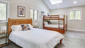 Un dormitorio con una cama grande, una litera y un tragaluz, además de varias ventanas.