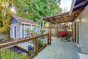 Eine Holzterrasse mit Schaukelstuhl, einem kleinen Schuppen und einem umzäunten Garten.