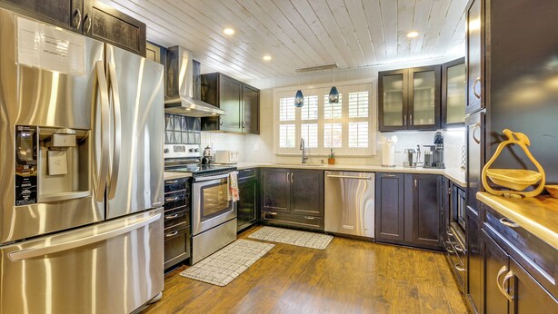 Una cocina moderna con electrodomésticos de acero inoxidable, suelo de madera y armarios oscuros.